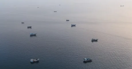 Vaporase ancorate pe o apă liniștită, simbolizând tensiuni în transportul maritim.