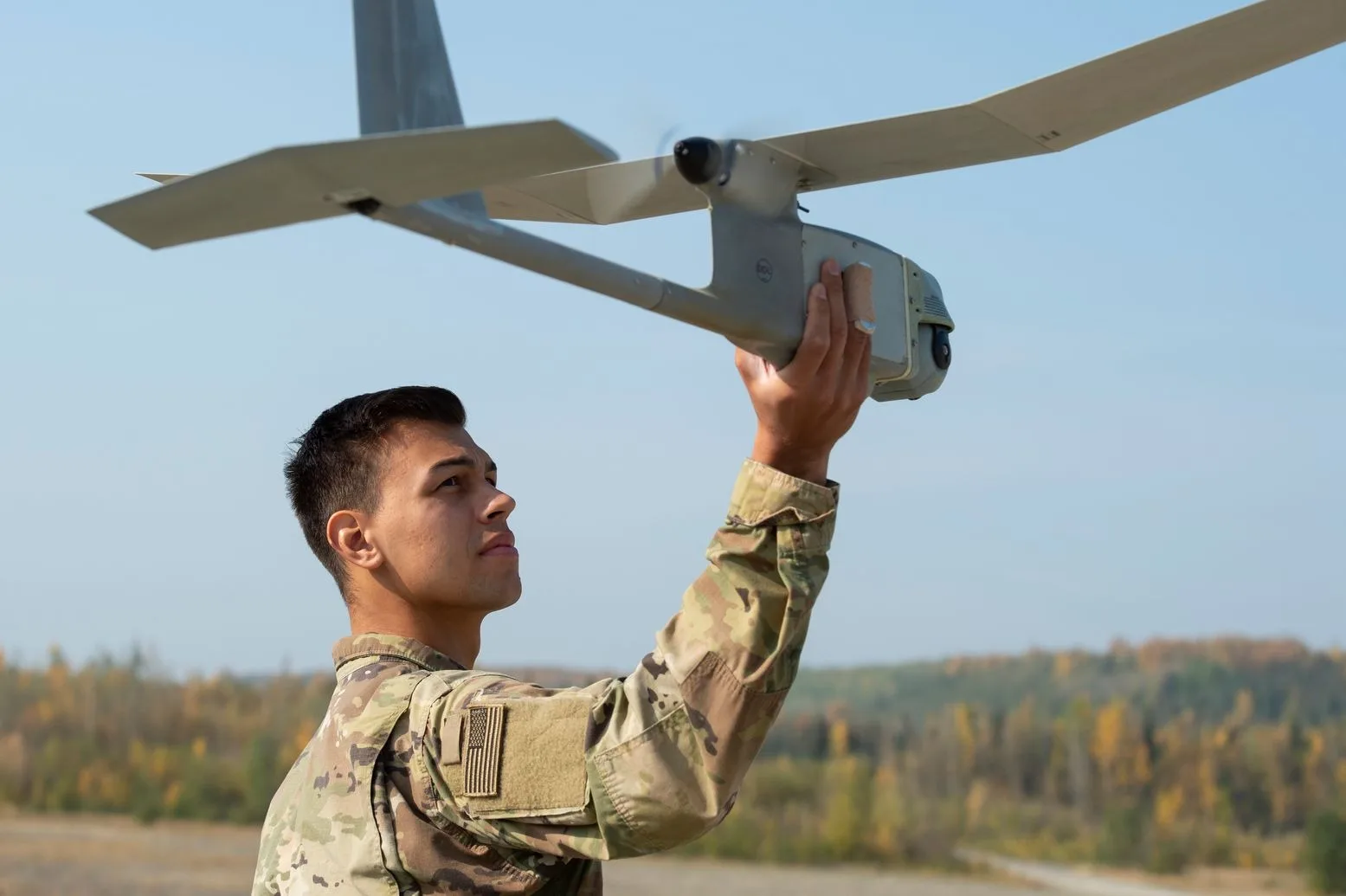 Un soldat pregătește o dronă pentru zbor într-un peisaj militar.