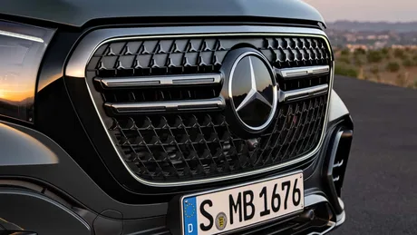 Grila distinctivă a unui vehicul Mercedes-Benz pe fundal urban.