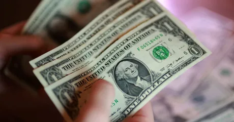 Bancnote de dolari americani în mână, simbolizând fluctuațiile valutare.