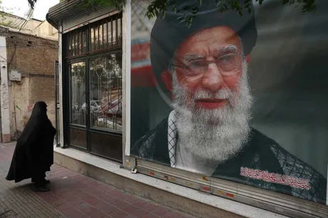 O femeie înveșmântată în negru trece pe lângă un portret al lui Ali Khamenei.