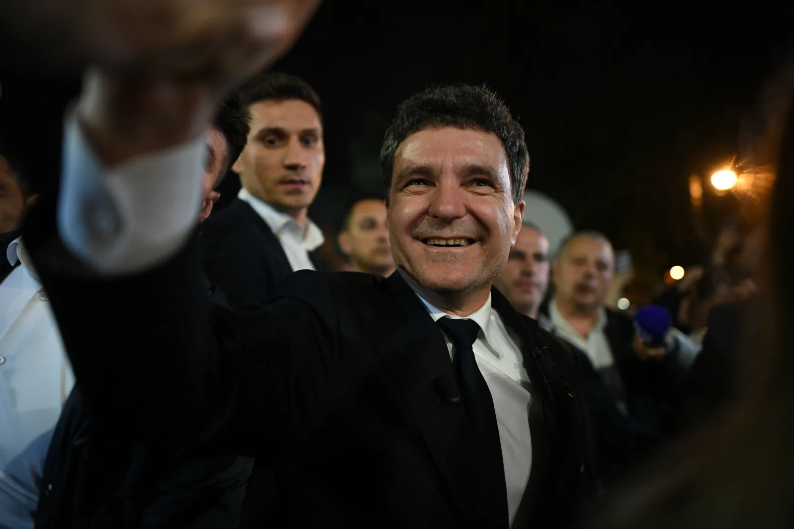 Dominic Fritz zâmbește și salută susținătorii într-un cadru politic agitat.
