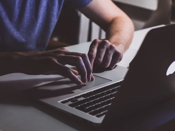 Utilizator scriind pe un laptop în întuneric, concentrat pe activitate.