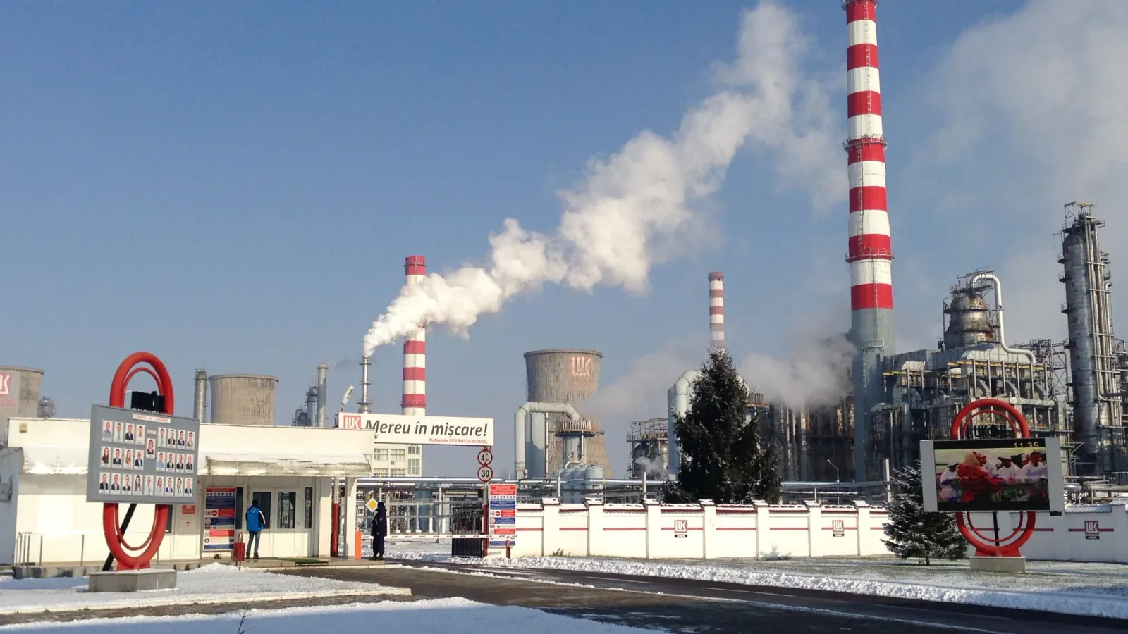 Rafinăria Petrotel în timpul unei zile însorite, cu fum ieșind din coșuri.