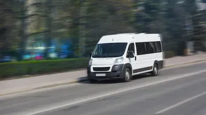 Autobuz alb circulând pe o stradă din România.