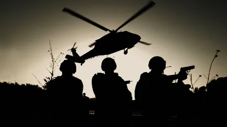 Silhouette de soldați și un elicopter în zbor la apus.