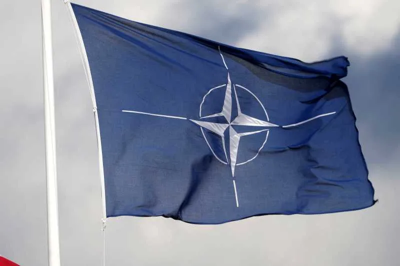 Steag NATO fluturând în vânt, simbol al cooperării internaționale.