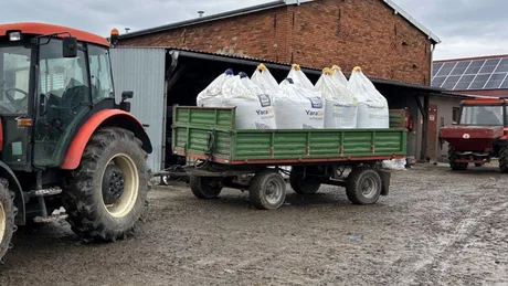 Tractor transportând saci cu îngrășăminte pe un teren agricol umed.