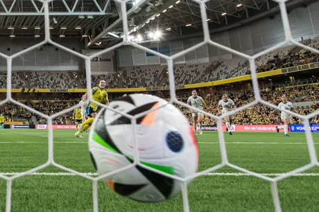 Minge de fotbal în apropierea porții, cu jucători pe teren.
