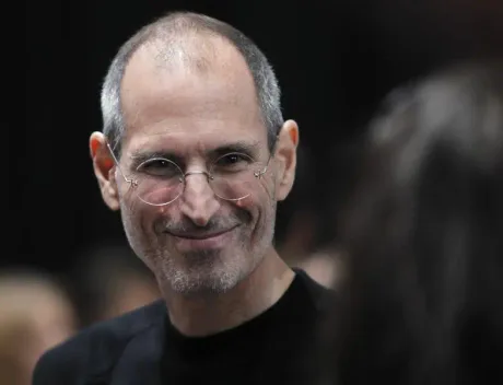 Steve Jobs zâmbind, într-un mediu de conferință tehnologică.