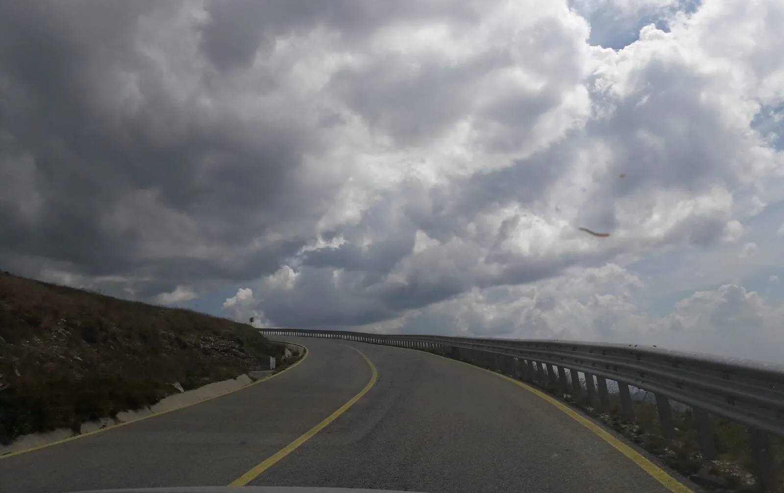 Peisaj montan pe Transfăgărășan, drum curbat și nori deasupra.