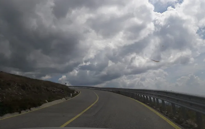 Peisaj montan pe Transfăgărășan, drum curbat și nori deasupra.