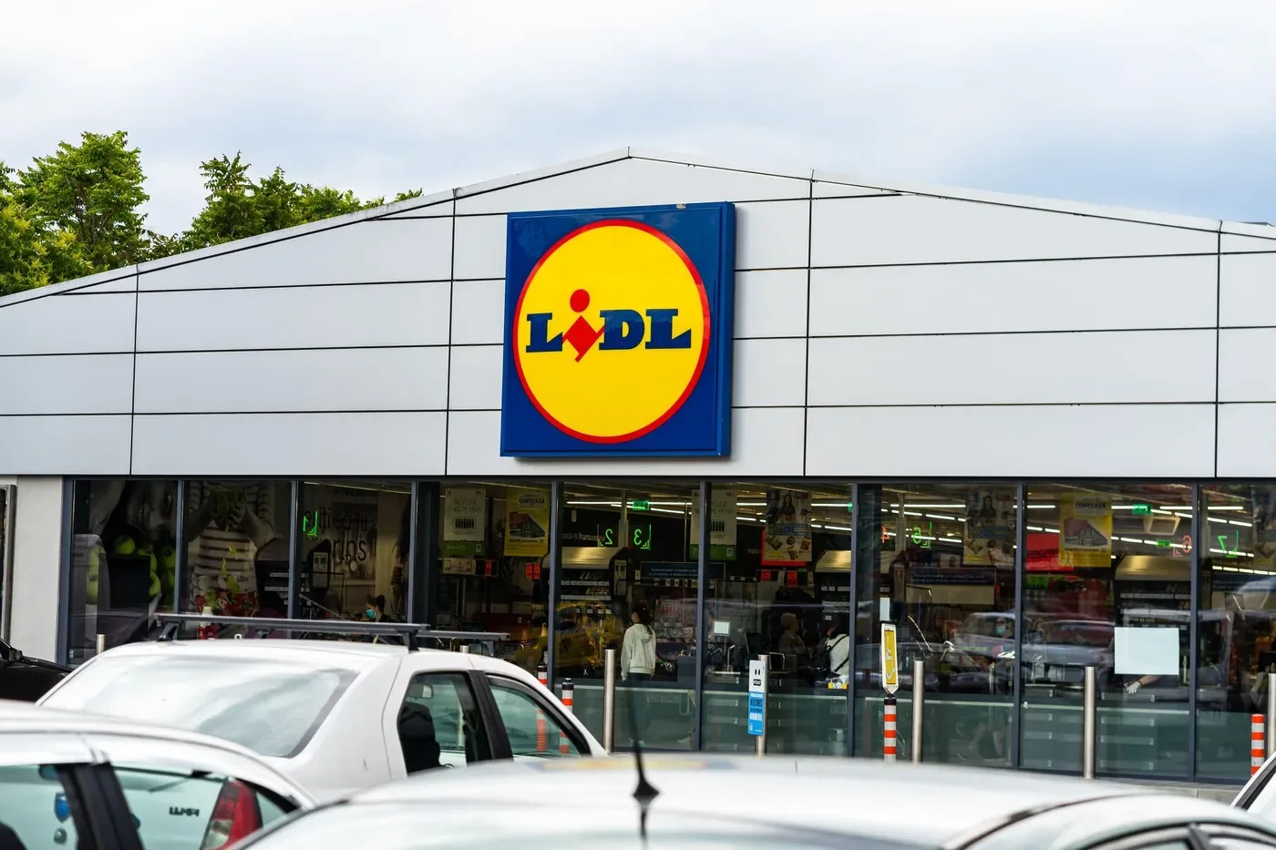Magazin Lidl cu clienți și mașini parcate în față.