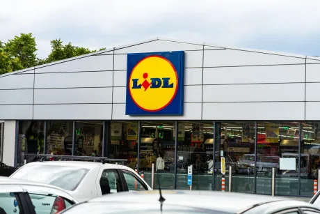 Magazin Lidl cu clienți și mașini parcate în față.