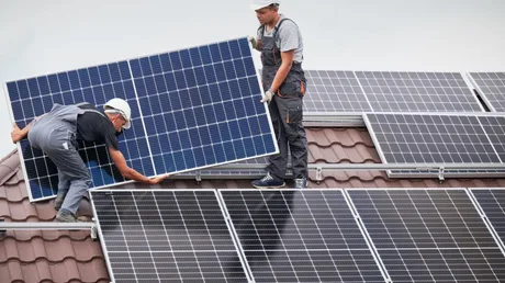 Instalare de panouri fotovoltaice pe o acoperiș, cu muncitori la lucru.