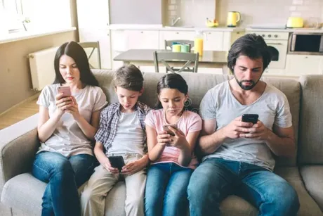 Familie utilizând telefoane mobile pe canapea, concentrată pe ecrane.