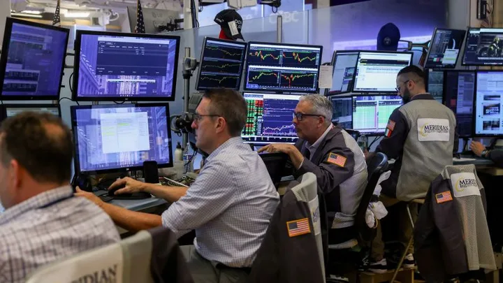 Traderi analizați piețele financiare în fața ecranelor multiple.