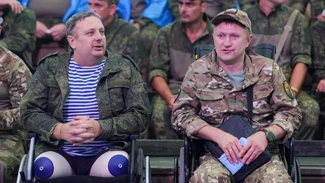 Doi bărbați în scaune cu rotile, discutând într-un mediu militar.