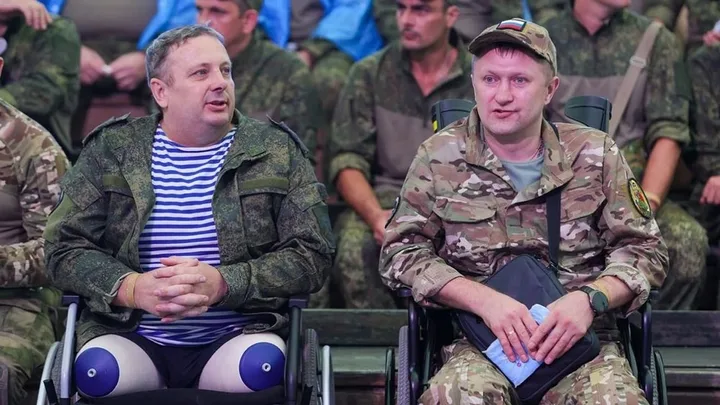 Doi bărbați în scaune cu rotile, discutând într-un mediu militar.