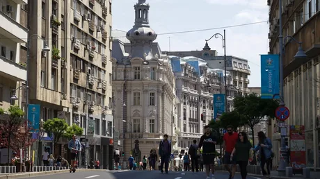 Stradă aglomerată din București, cu clădiri istorice și oameni pe trotuar.
