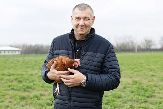 Producător local cu o pasăre în brațe, pe câmp verde.