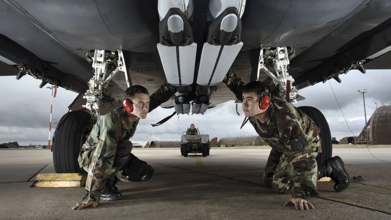 Doi soldați inspectează un avion militar pe o pistă de decolare.