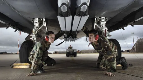 Doi soldați inspectează un avion militar pe o pistă de decolare.