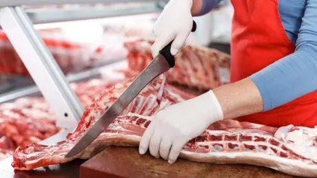 Un muncitor taie carne într-un abator modern din România.