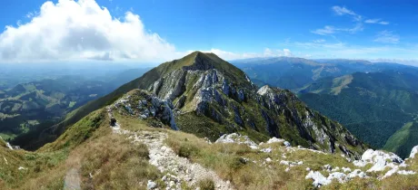 Peisaj montan cu vârfuri acoperite de iarbă și stânci, cer senin.