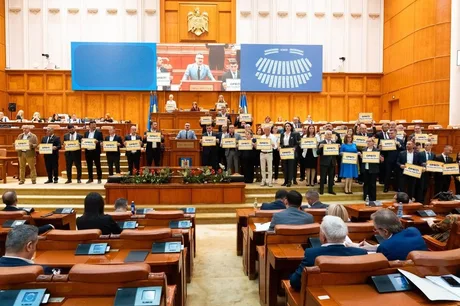 Parlamentarii AUR protestează cu pancarte în plenul Parlamentului.