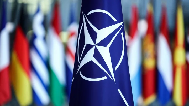 Steagul NATO în fața unor drapele naționale diverse.