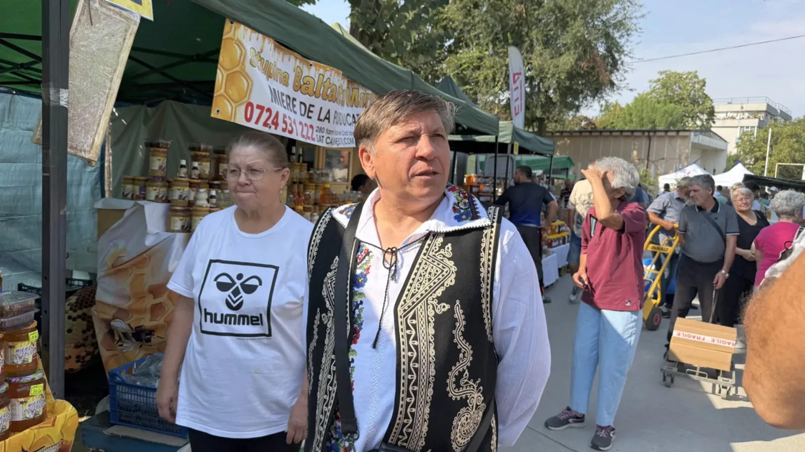 Apicultor la târg, vânzând miere din Olt, cu costume tradiționale.