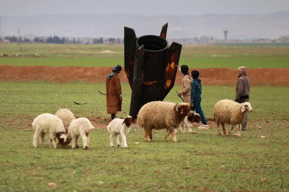 Copii se joacă în jurul unei rachete căzute, înconjurați de oi pe câmpul din Siria.