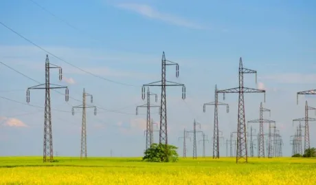 Stâlpi de electricitate pe un câmp verde sub un cer senin.