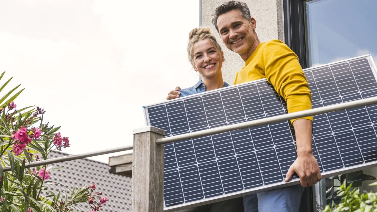 Cuplu fericit ținând un panou solar pe balcon.