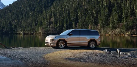 Un SUV modern parcat lângă un lac, înconjurat de pădure de conifere.