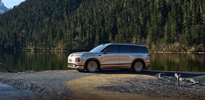 Un SUV modern parcat lângă un lac, înconjurat de pădure de conifere.