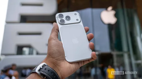 Un smartphone Apple este ținut în mână, cu logo-ul Apple vizibil în fundal.