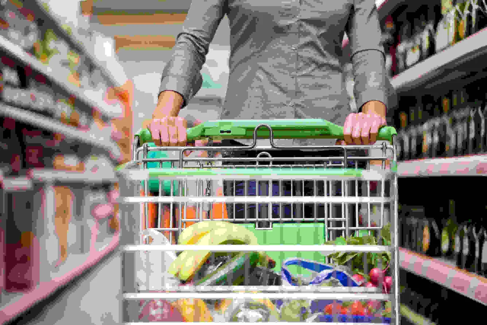 Persoană cu un cărucior de cumpărături plin de alimente în supermarket.