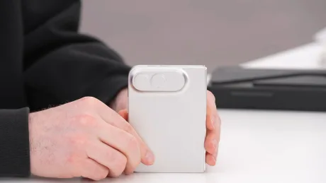 Un telefon mobil alb, ținut în mână, pe un birou alb.