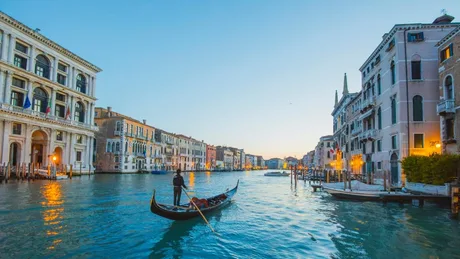 Veneția la apus, cu gondole pe canal și clădiri istorice.
