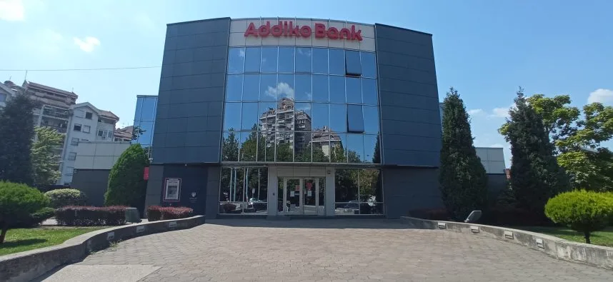 Clădirea Addiko Bank reflectă cerul albastru și vegetația din jur.