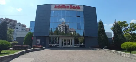 Clădirea Addiko Bank reflectă cerul albastru și vegetația din jur.