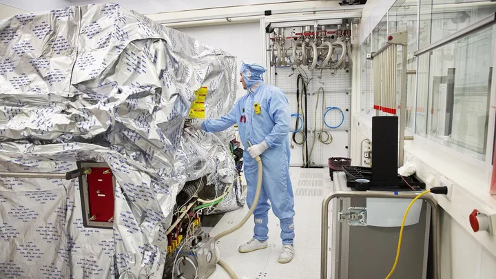 Un tehnician în echipament de protecție lucrează într-o fabrică de semiconductori.