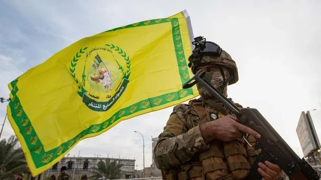 Un luptător Hezbollah cu steagul organizației și armament în mână.