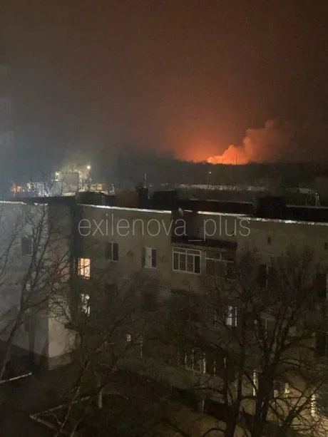 Explozie în fundal, pe un cer întunecat, lângă clădiri urbane.