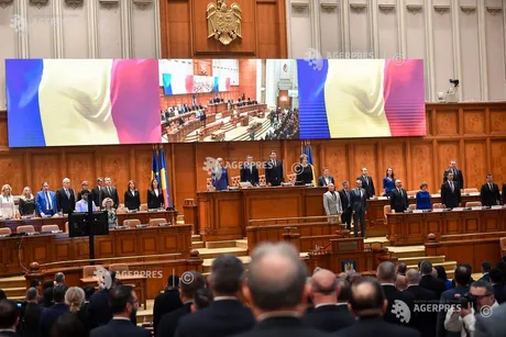 Parlamentarii stau în sala de ședințe, cu drapelul României în fundal.