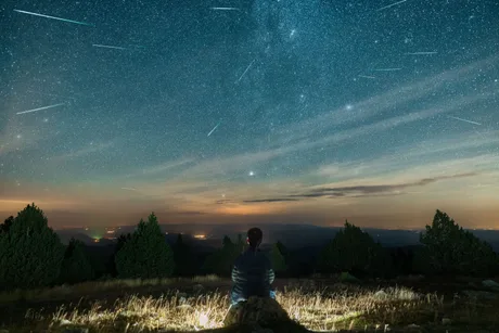Cerul plin de meteori în noaptea Perseidelor, observat dintr-o zonă întunecată.