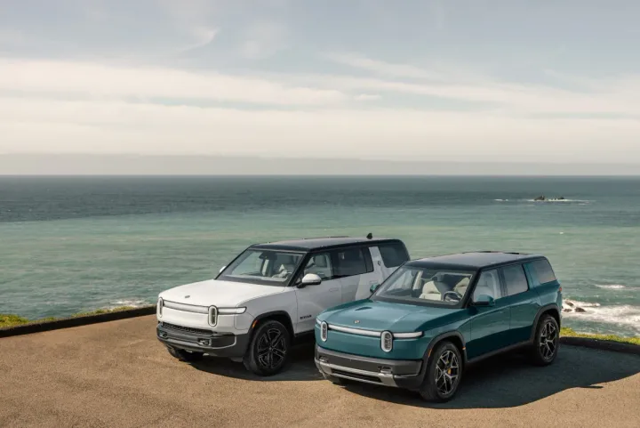 Două SUV-uri electrice Rivian R2 parcate pe malul mării, cu un peisaj panoramic în fundal.