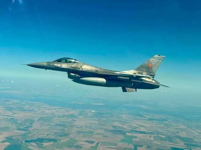 Un avion de luptă zboară deasupra unui peisaj rural vast.